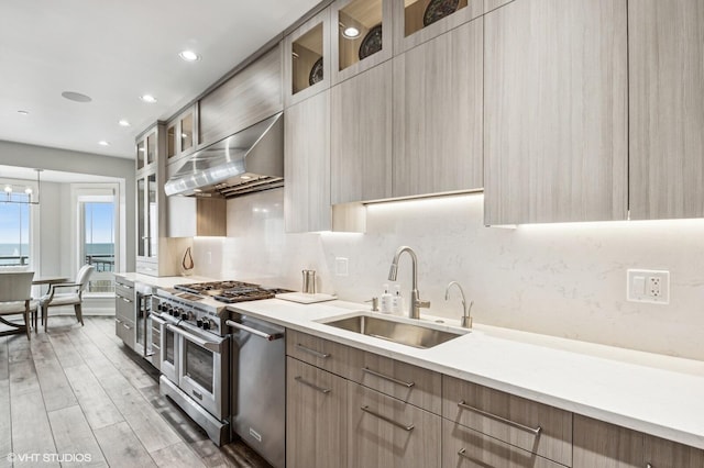 kitchen featuring modern cabinets, range hood, light countertops, a sink, and appliances with stainless steel finishes