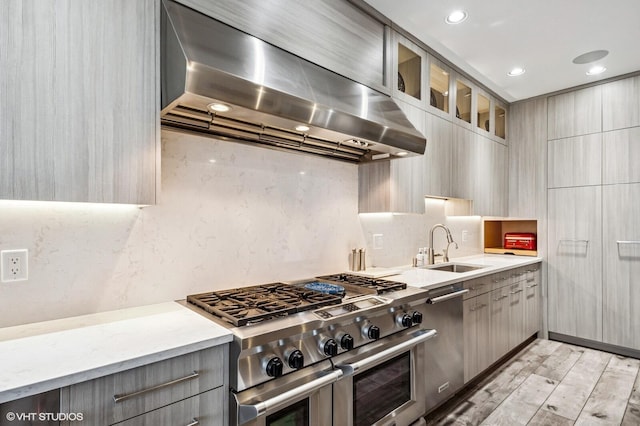 kitchen with wall chimney range hood, appliances with stainless steel finishes, a sink, gray cabinets, and modern cabinets