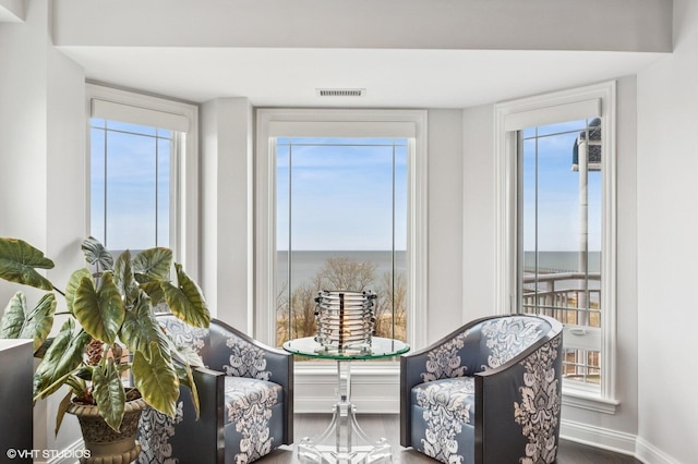 living area featuring visible vents, baseboards, a water view, and a healthy amount of sunlight