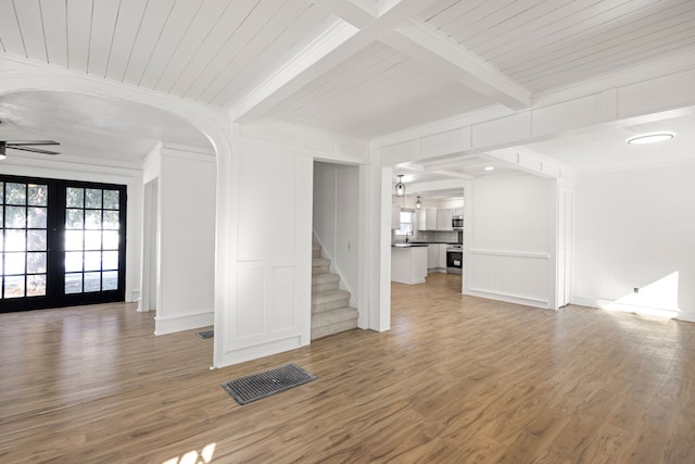 unfurnished living room featuring visible vents, a decorative wall, beamed ceiling, ceiling fan, and stairway