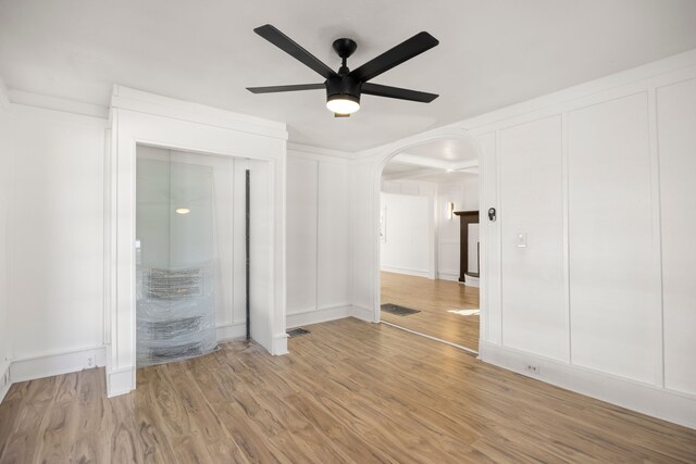 unfurnished bedroom featuring wood finished floors, arched walkways, a ceiling fan, and a decorative wall