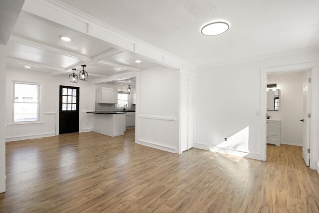 unfurnished living room featuring beamed ceiling, a notable chandelier, light wood-style floors, ornamental molding, and coffered ceiling