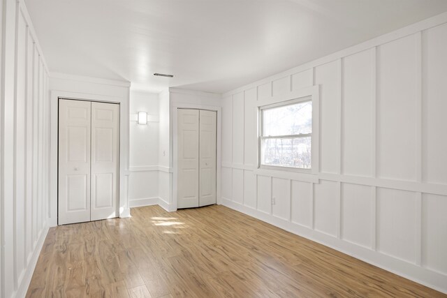 unfurnished bedroom with light wood-type flooring, multiple closets, crown molding, and a decorative wall