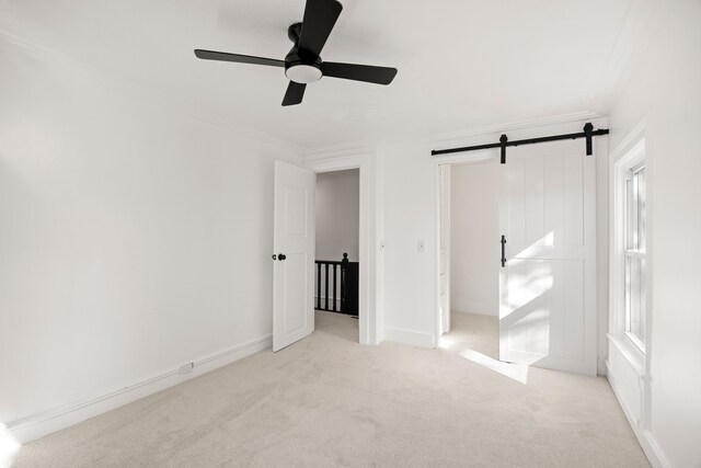 unfurnished bedroom featuring carpet floors, ornamental molding, a ceiling fan, and a barn door