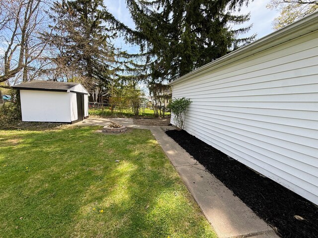 view of yard with a storage unit, a fire pit, fence, and an outbuilding