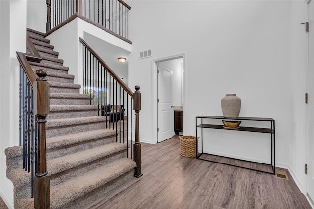staircase featuring a towering ceiling, baseboards, visible vents, and wood finished floors