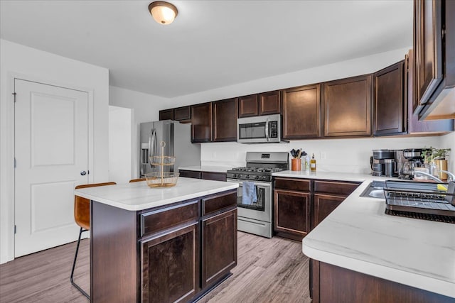 kitchen with light wood finished floors, a center island, stainless steel appliances, dark brown cabinetry, and light countertops