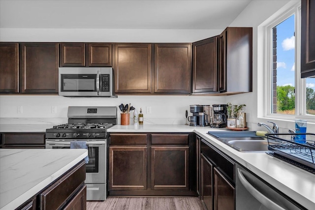 kitchen featuring dark brown cabinets, stainless steel appliances, light wood-style flooring, and a sink