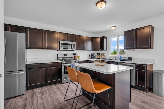 kitchen featuring dark brown cabinets, stainless steel appliances, a breakfast bar area, and light wood-type flooring