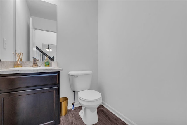 half bathroom featuring toilet, baseboards, wood finished floors, and vanity