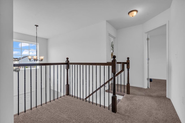 corridor featuring baseboards, a notable chandelier, an upstairs landing, and carpet