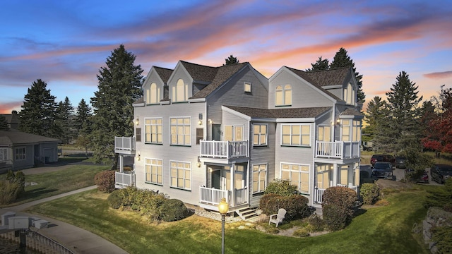 view of front of home with a lawn, cooling unit, a shingled roof, and a balcony