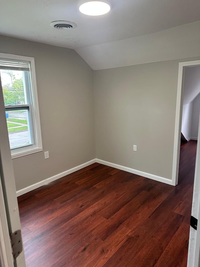 additional living space with baseboards, vaulted ceiling, dark wood-style floors, and visible vents