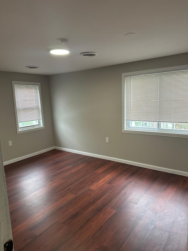 empty room with plenty of natural light, dark wood-style flooring, and baseboards