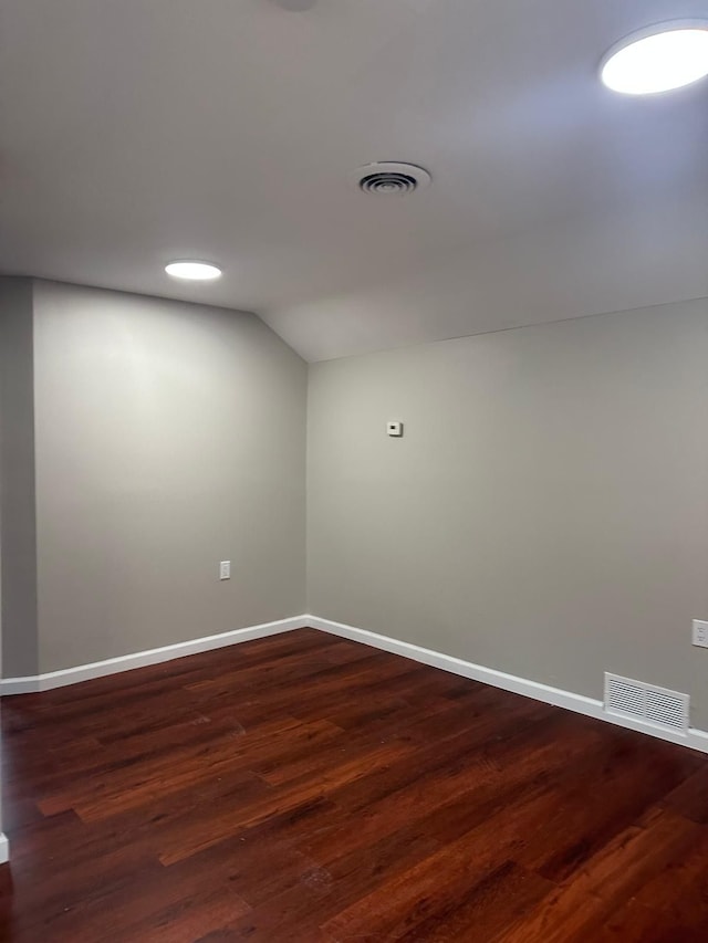 spare room featuring baseboards, lofted ceiling, dark wood-style flooring, and visible vents