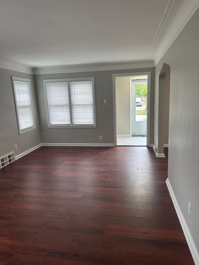 empty room featuring dark wood-style flooring, arched walkways, baseboards, and visible vents