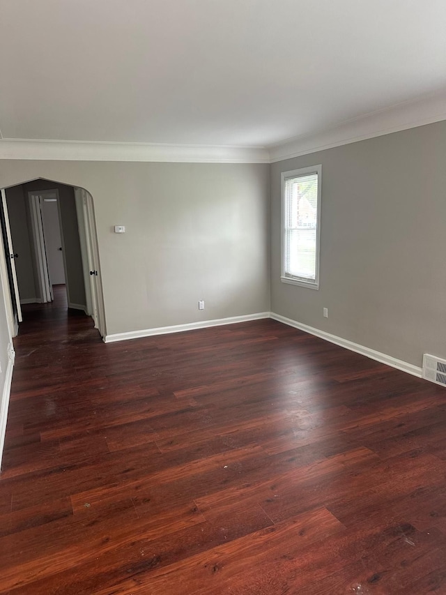 empty room with dark wood-style flooring, arched walkways, baseboards, visible vents, and ornamental molding