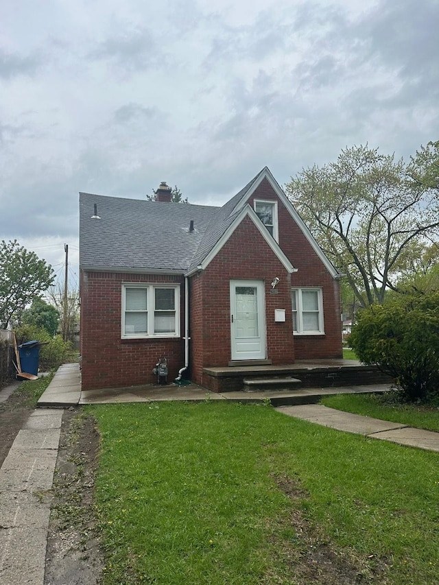 bungalow-style house featuring a shingled roof, a chimney, a front yard, and brick siding