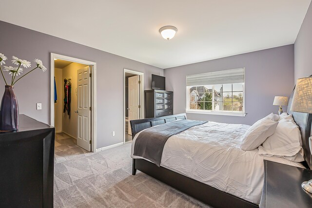 bedroom featuring baseboards, a walk in closet, a closet, and light carpet