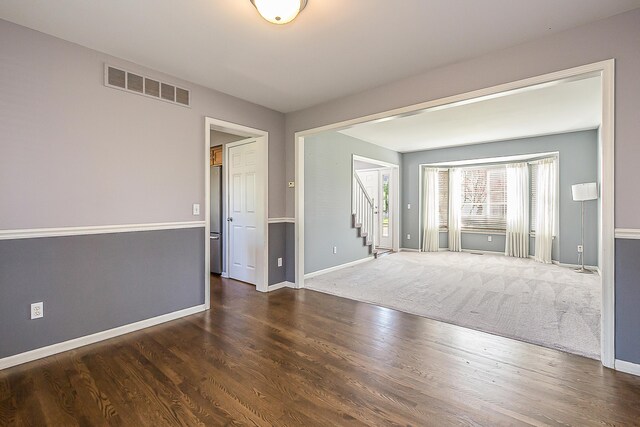 spare room with stairway, baseboards, wood finished floors, and visible vents