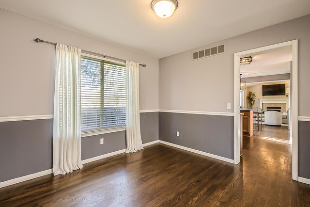 unfurnished room with visible vents, baseboards, dark wood-type flooring, and a fireplace