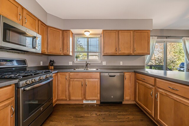 kitchen featuring brown cabinets, dark countertops, appliances with stainless steel finishes, a sink, and dark wood-type flooring
