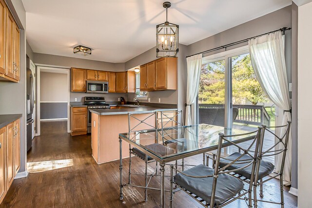 kitchen featuring dark countertops, appliances with stainless steel finishes, a sink, dark wood finished floors, and baseboards