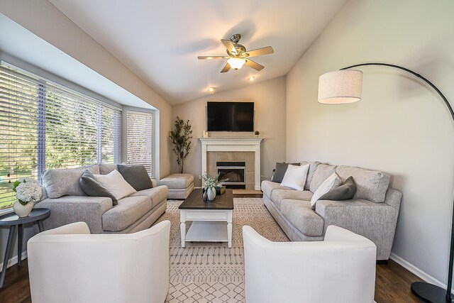 living area featuring wood finished floors, baseboards, a tiled fireplace, a ceiling fan, and vaulted ceiling