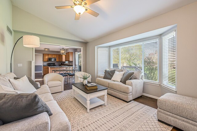 living room with visible vents, baseboards, a ceiling fan, light wood-style flooring, and vaulted ceiling