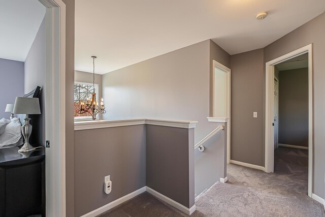 hallway featuring carpet floors, baseboards, a chandelier, and an upstairs landing