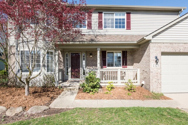 traditional-style home featuring covered porch, an attached garage, and brick siding