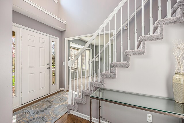 foyer featuring baseboards, a high ceiling, stairs, and wood finished floors