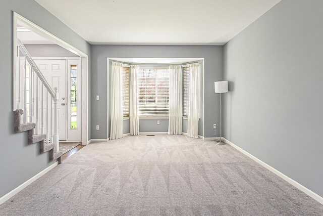 carpeted empty room with baseboards and stairs