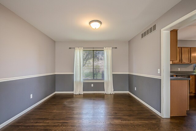 empty room featuring visible vents, baseboards, and dark wood-style floors