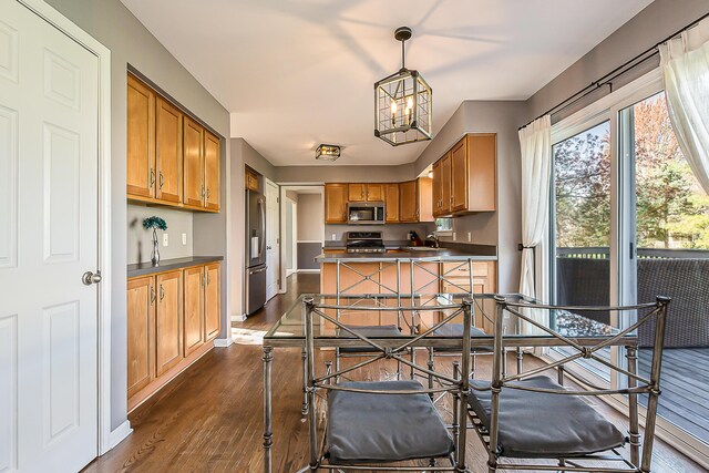 kitchen with dark countertops, brown cabinets, dark wood finished floors, a chandelier, and stainless steel appliances