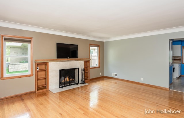 unfurnished living room with visible vents, a tile fireplace, baseboards, ornamental molding, and light wood-style flooring