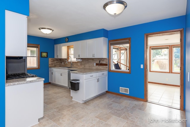 kitchen with white cabinets, backsplash, baseboards, and a sink