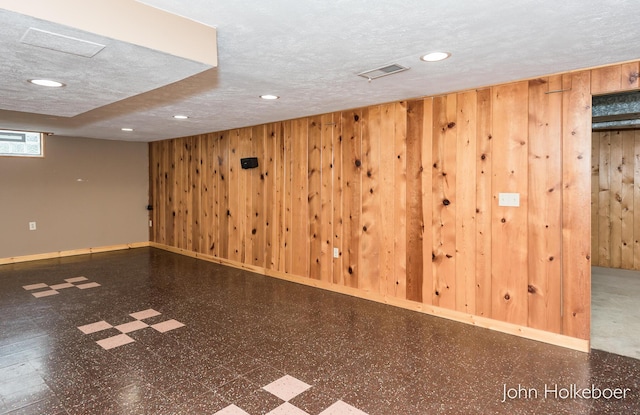 below grade area with tile patterned floors, wood walls, and visible vents