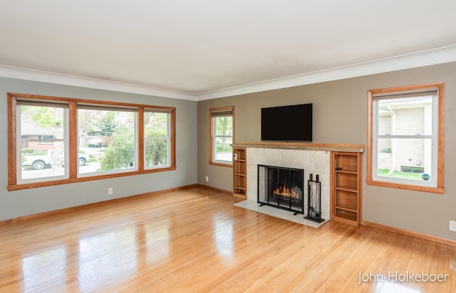 unfurnished living room with baseboards, a high end fireplace, wood finished floors, and a healthy amount of sunlight
