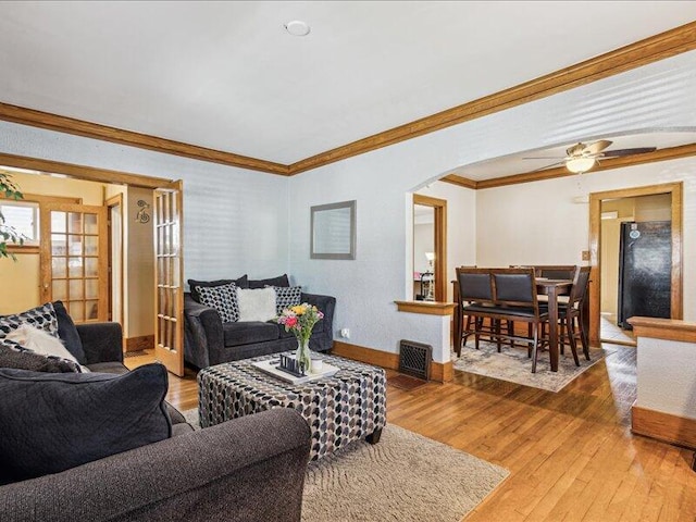 living area with wood-type flooring, arched walkways, baseboards, and ornamental molding