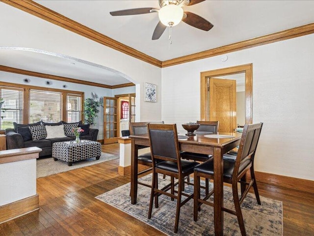 dining area featuring arched walkways, ornamental molding, wood-type flooring, and ceiling fan