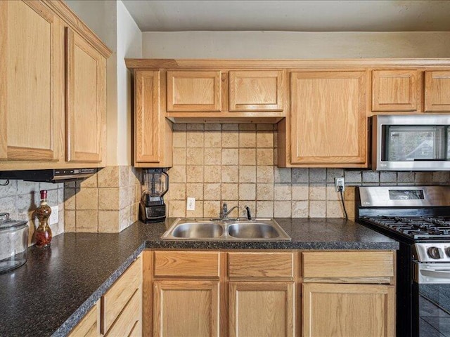 kitchen featuring dark countertops, appliances with stainless steel finishes, a sink, light brown cabinets, and decorative backsplash