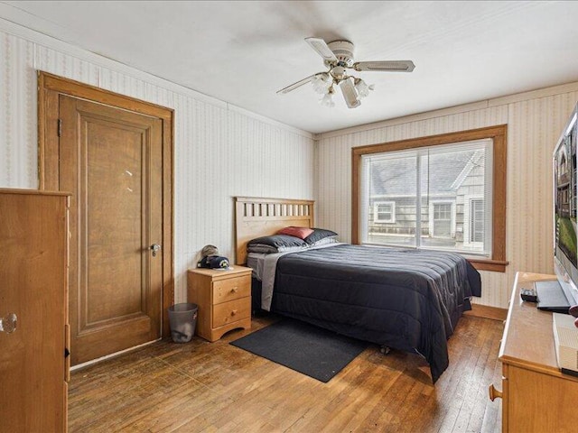 bedroom with crown molding, a ceiling fan, wallpapered walls, and hardwood / wood-style floors