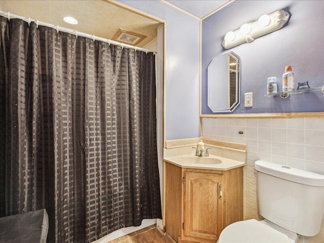 bathroom with wainscoting, vanity, toilet, tile walls, and visible vents