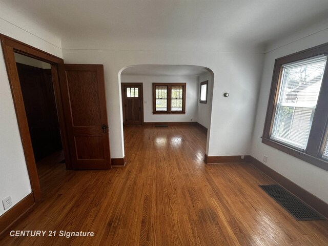interior space with arched walkways, baseboards, wood finished floors, and visible vents