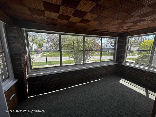 unfurnished sunroom featuring brick wall, a wealth of natural light, and carpet