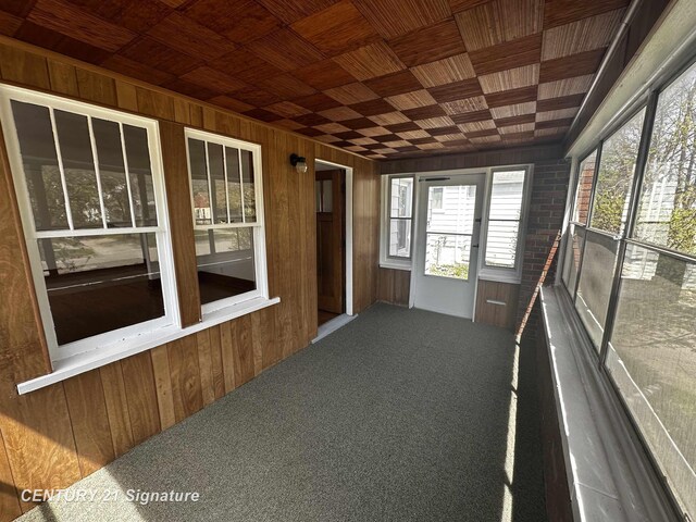 unfurnished sunroom with carpet floors, wood walls, and a wealth of natural light