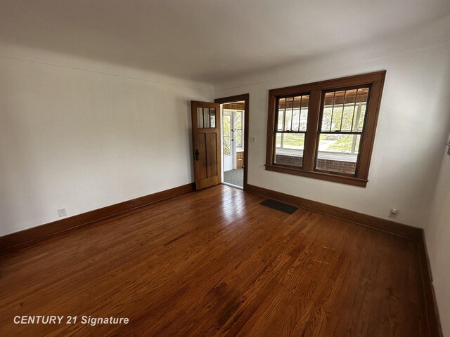 unfurnished room featuring baseboards, a wealth of natural light, dark wood-type flooring, and visible vents