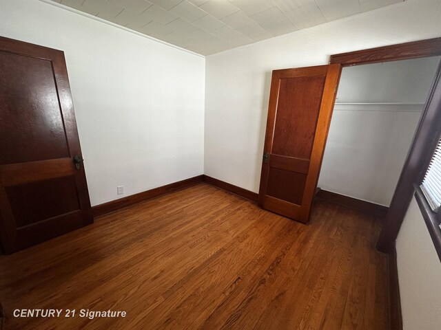 unfurnished bedroom featuring baseboards, dark wood-style floors, and a closet
