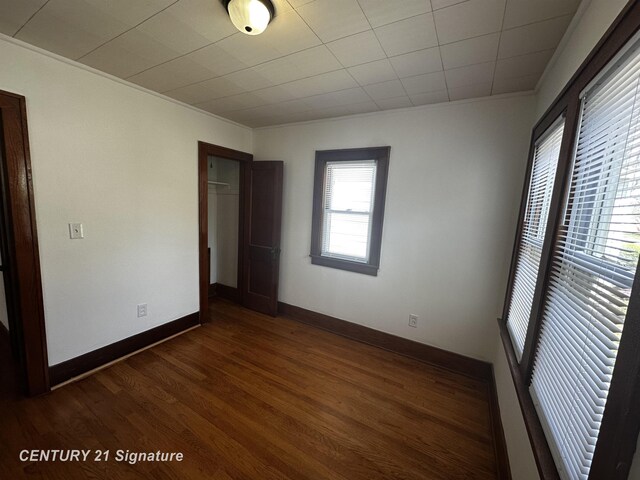 unfurnished bedroom featuring a closet, ornamental molding, dark wood finished floors, and baseboards